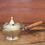 Brass incense burner with wooden handle on a wooden surface