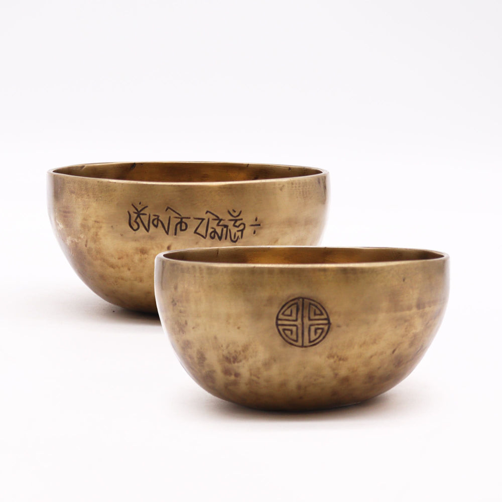 Two brass singing bowls with engravings on a white background