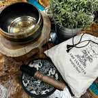 Tibetan singing bowl set with wooden mallet and pouch on a wooden surface.