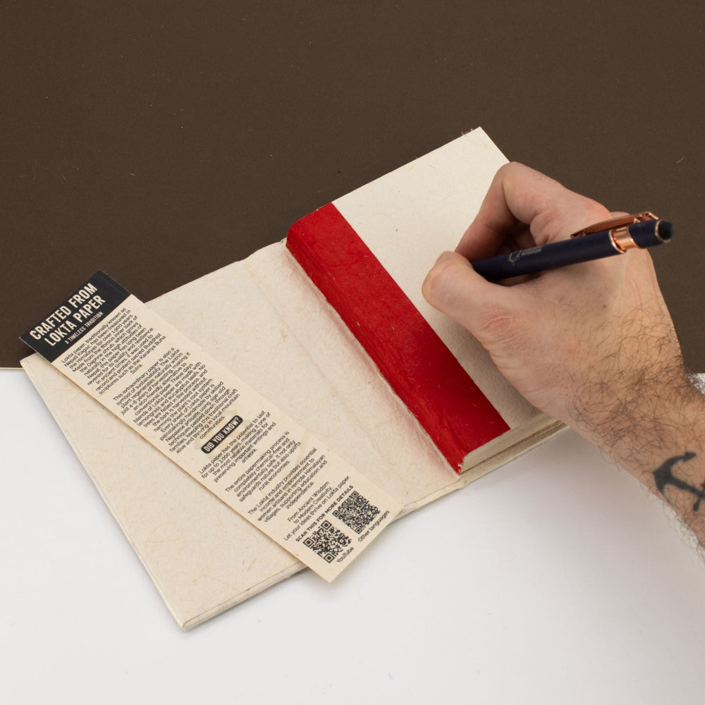 Hand writing in a notebook with a red stripe on a white surface