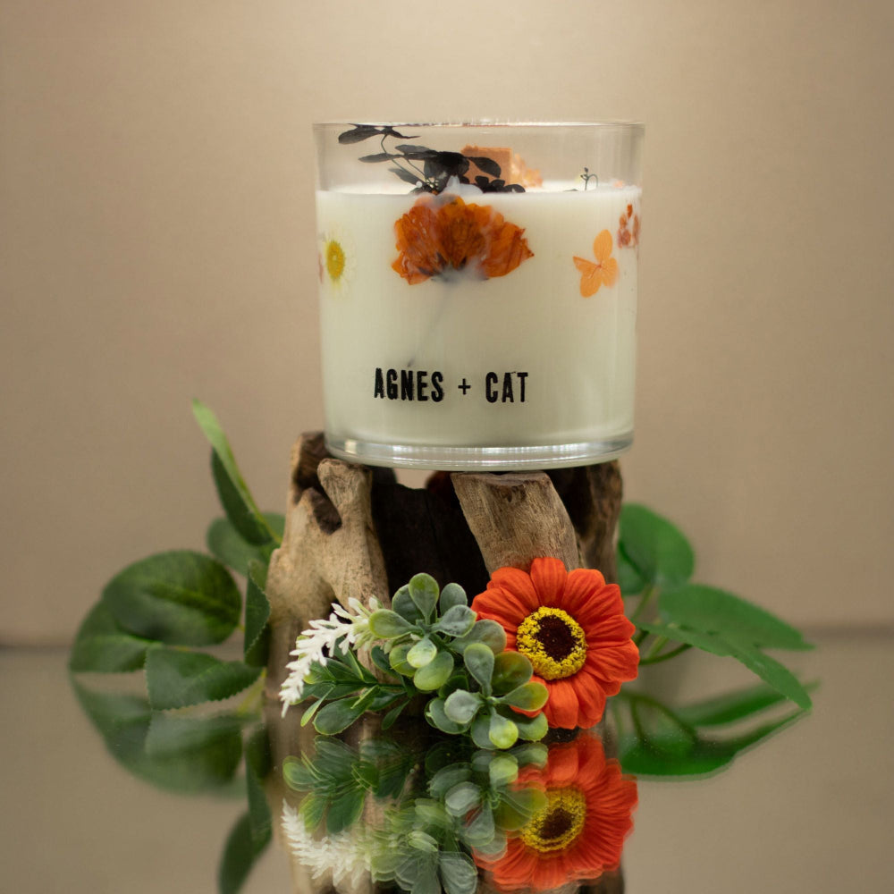Candle in a glass jar with floral design on a wooden block, featuring the brand 'AGNES + CAT'.
