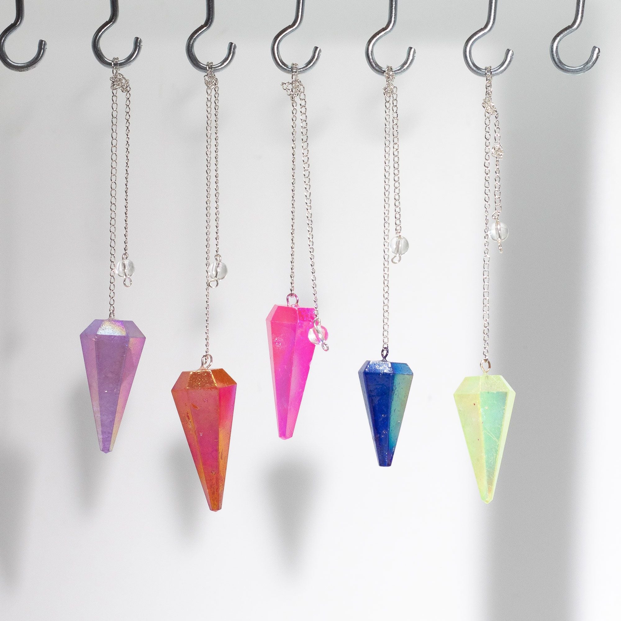 Colorful crystal pendulums hanging from hooks on a white background