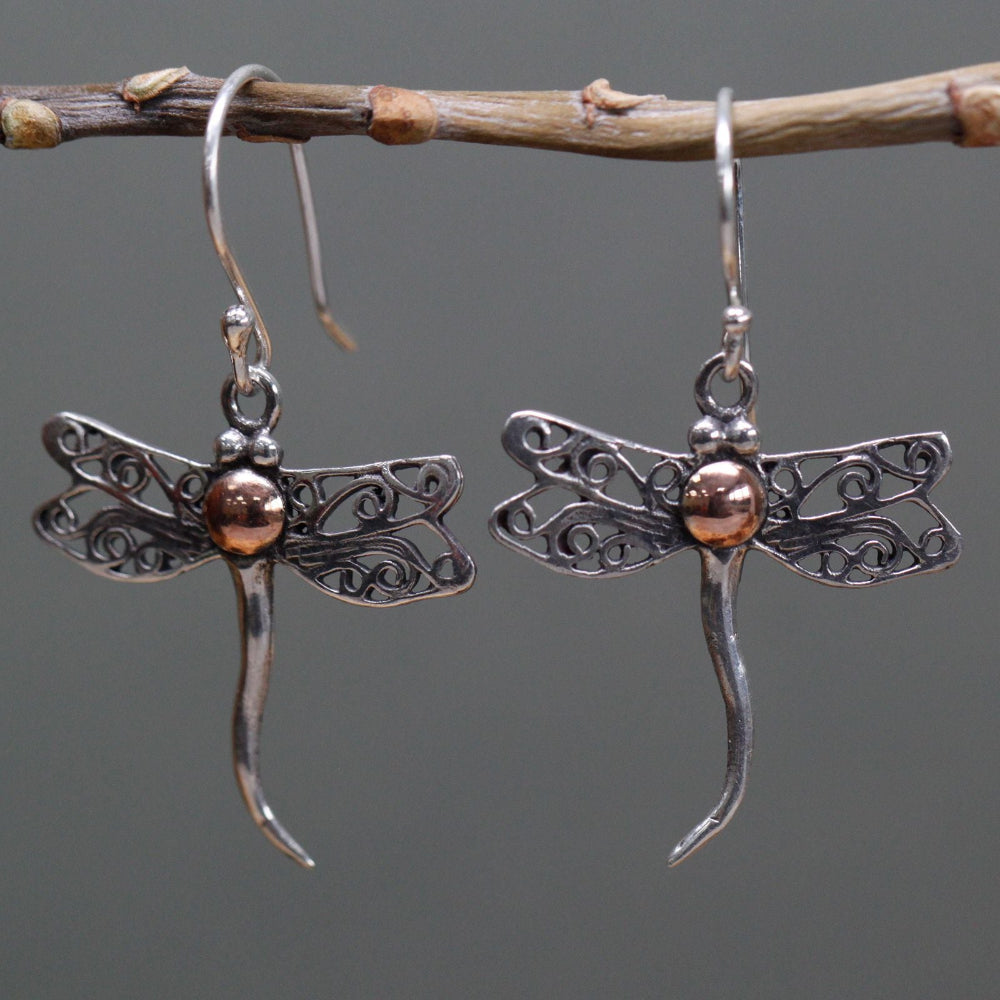 Dragonfly-shaped earrings on a branch with a gray background