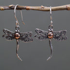 Dragonfly-shaped earrings on a branch with a gray background