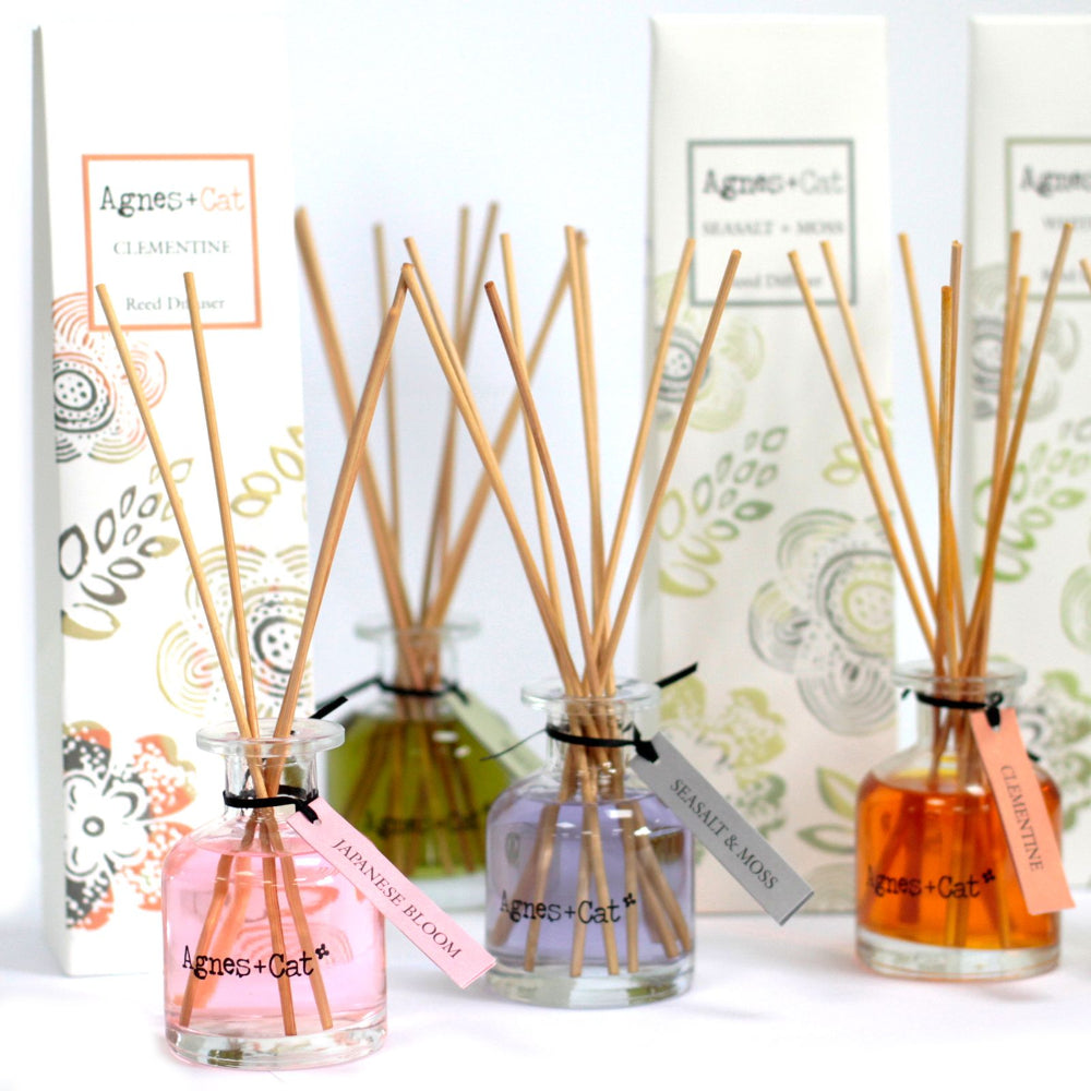 Three diffuser bottles with wooden sticks and colorful packaging on a white background