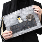 Person holding a gray felt pouch with embroidered penguin and dog design.