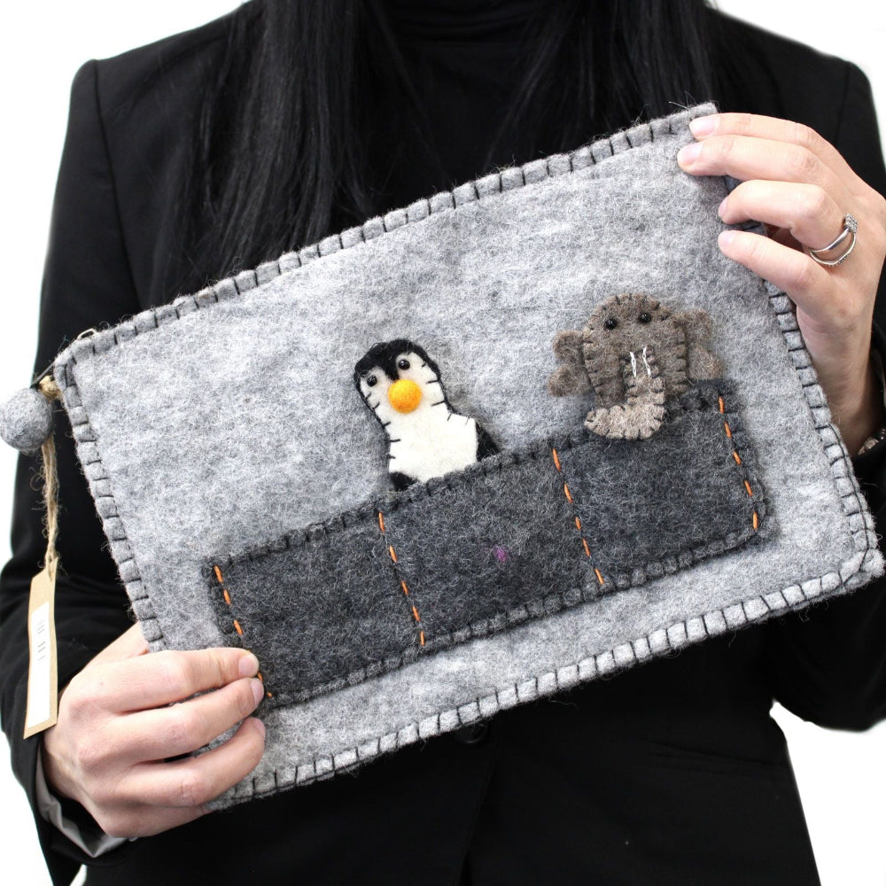 Person holding a gray felt pouch with embroidered penguin and dog design.