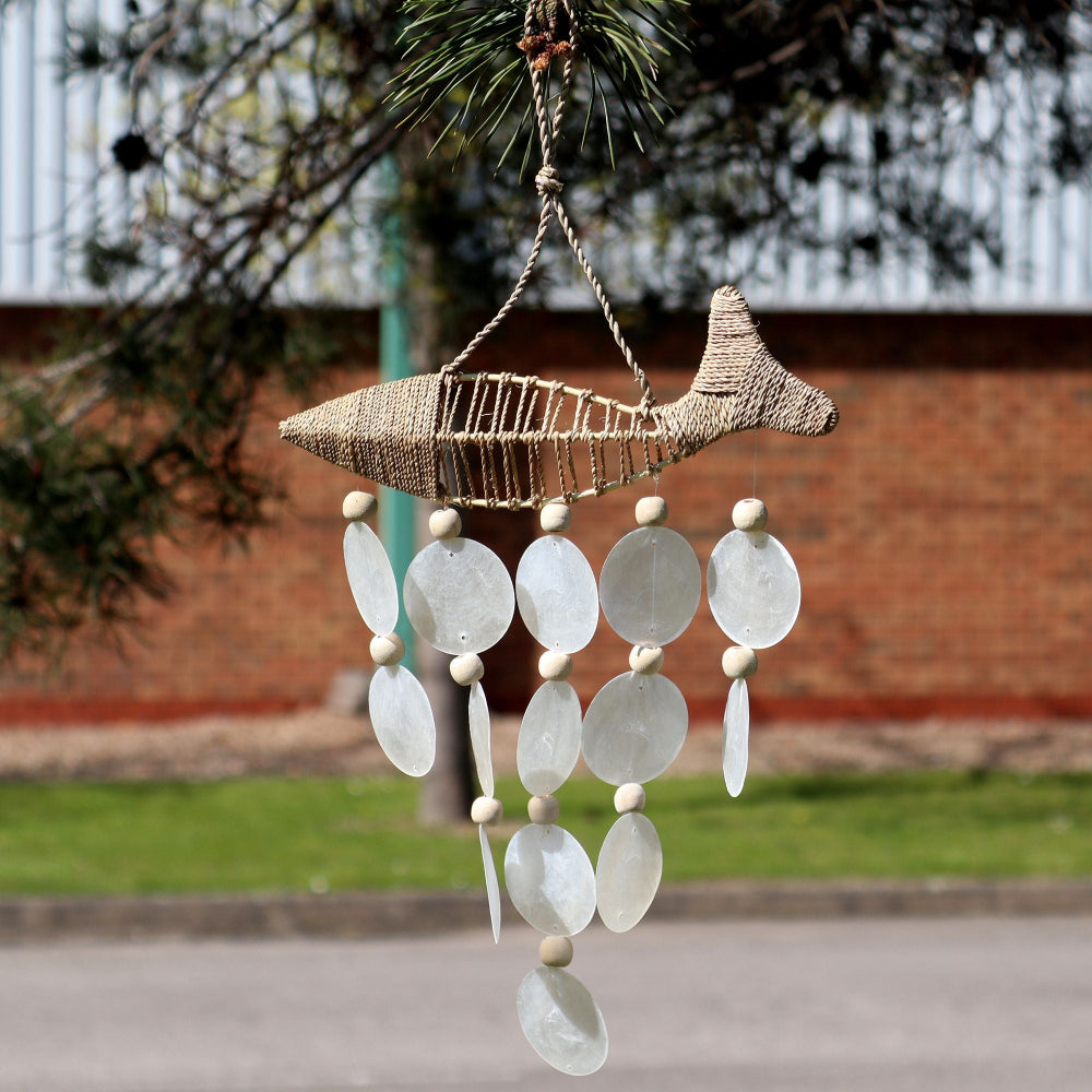 Decorative fish-shaped wind chime with shell-like beads hanging outdoors.