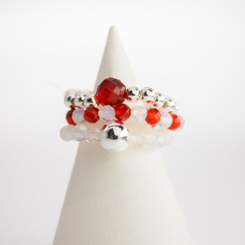 Stack of red and silver beaded rings on a white cone-shaped stand against a white background