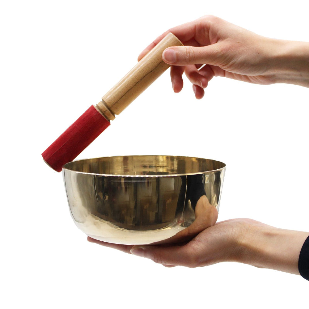 Gold singing bowl held by a hand with a wooden and red-mitten striker on a white background