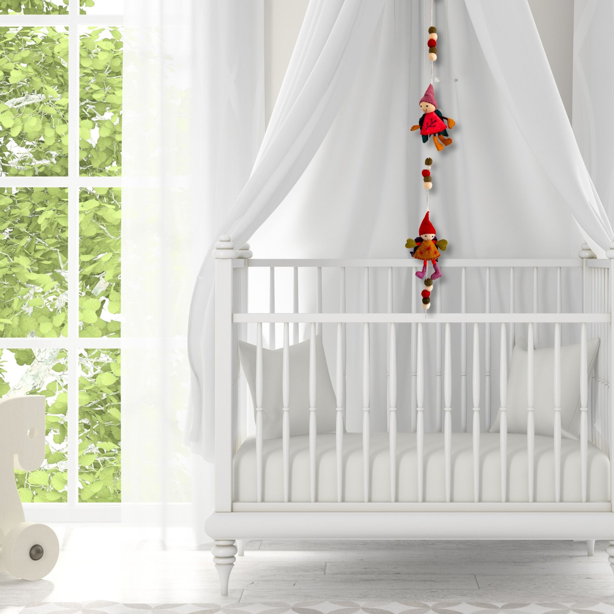 White crib with canopy and hanging gnome decorations in a bright room with large windows.