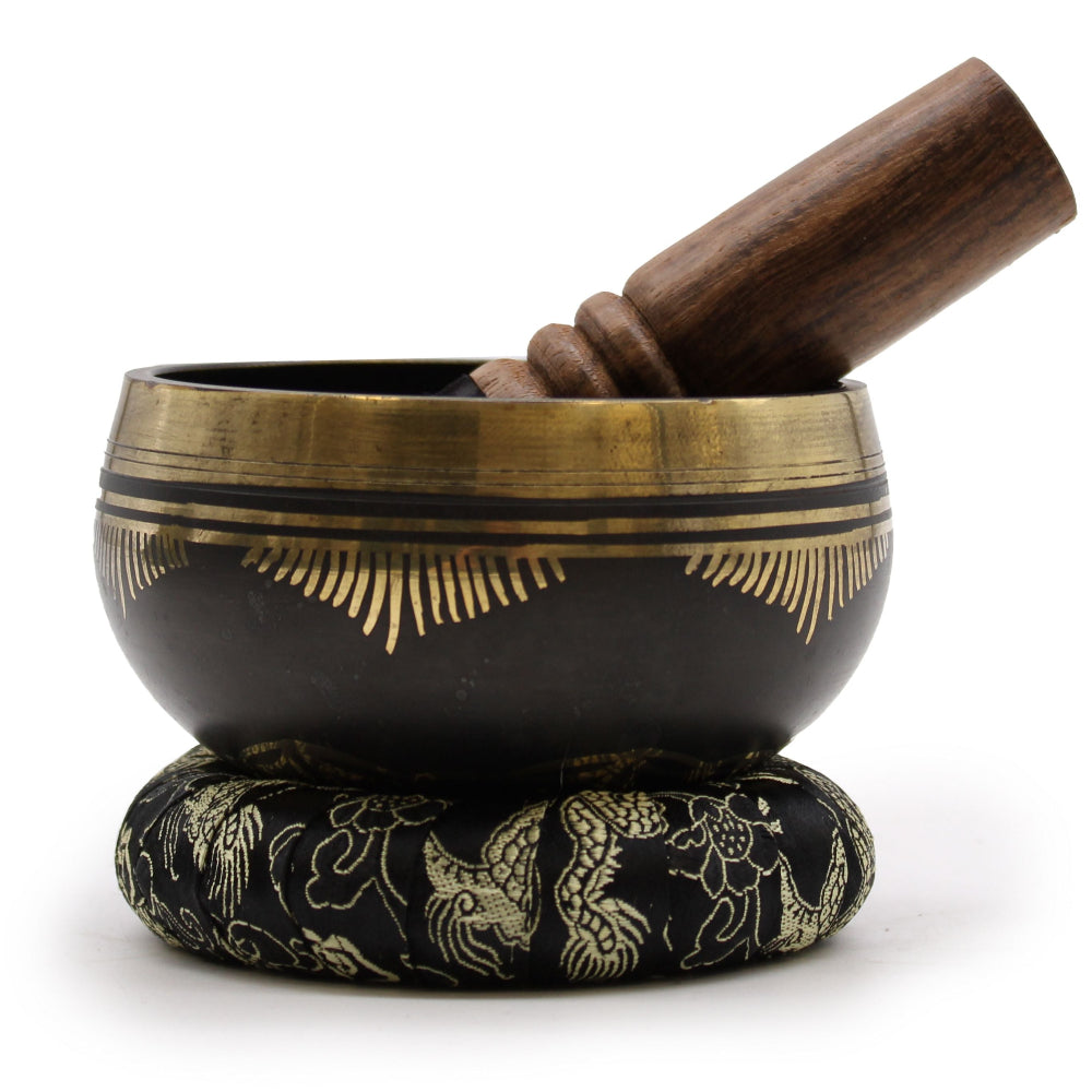 Black singing bowl with gold accents and wooden striker on a white background