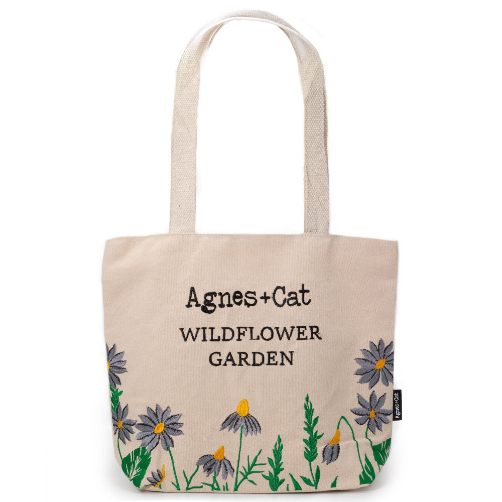 Beige tote bag with floral designs and 'Agnes + Cat Wildflower Garden' text on a white background