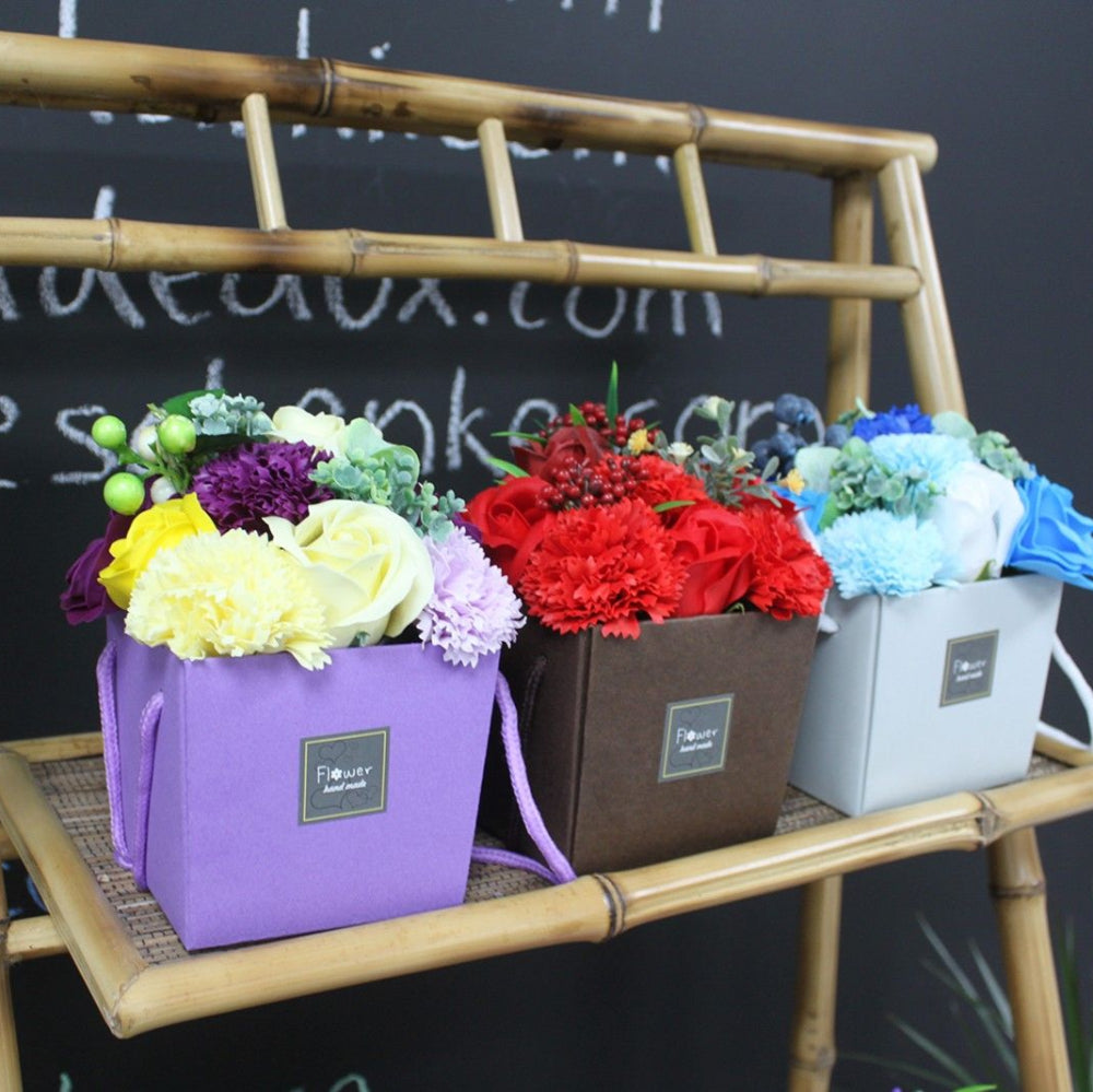 Three flower arrangements in colorful boxes on a bamboo stand against a chalkboard background.