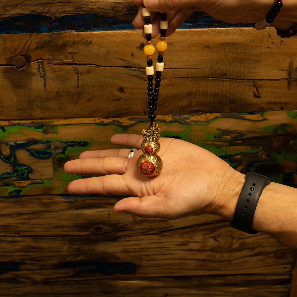 Hand holding a beaded necklace with a decorative pendant against a wooden background