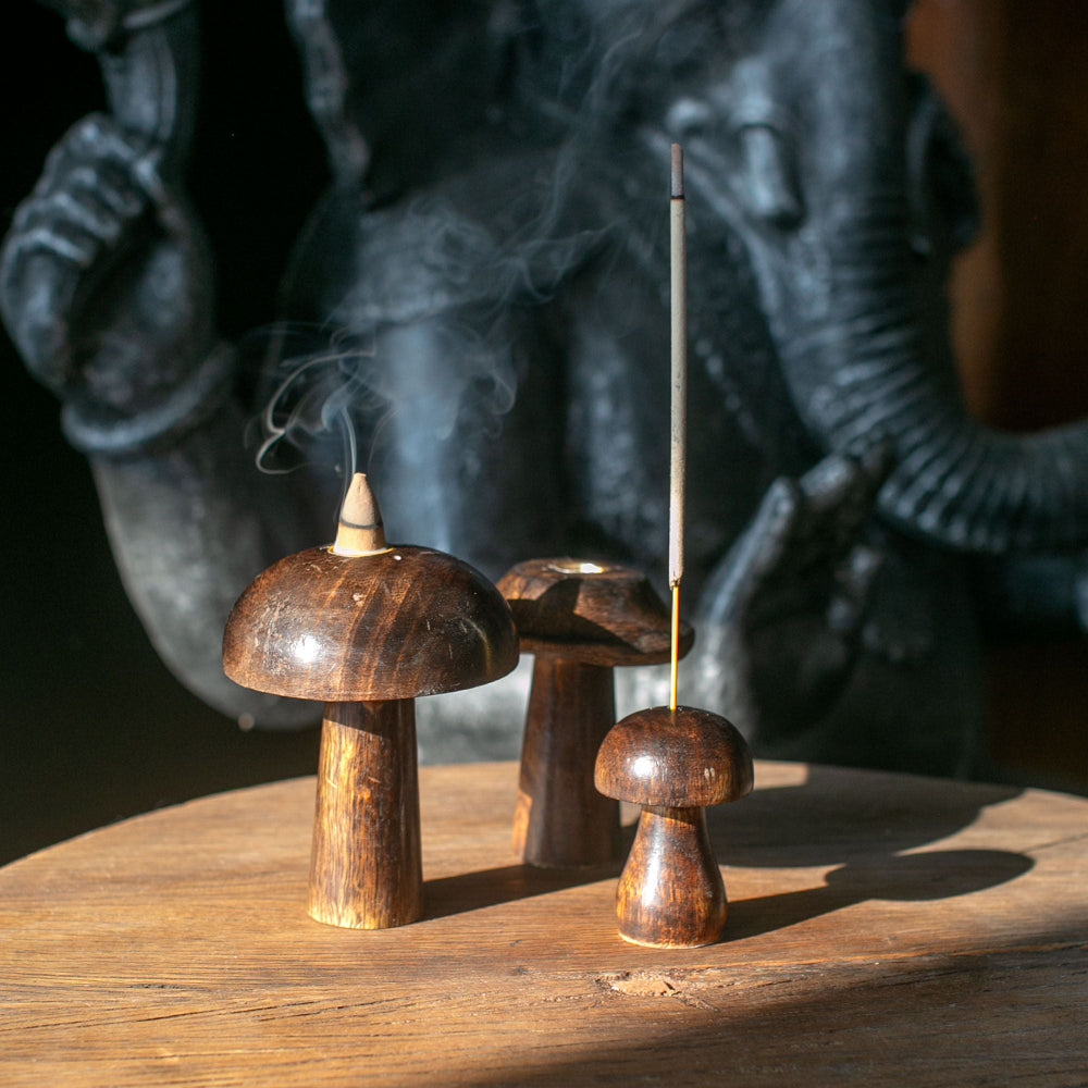 Wooden mushroom-shaped incense holders with incense sticks on a wooden surface, with a dark background.
