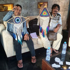 Two people sitting on a couch holding colorful dream catchers, with a table in front of them.