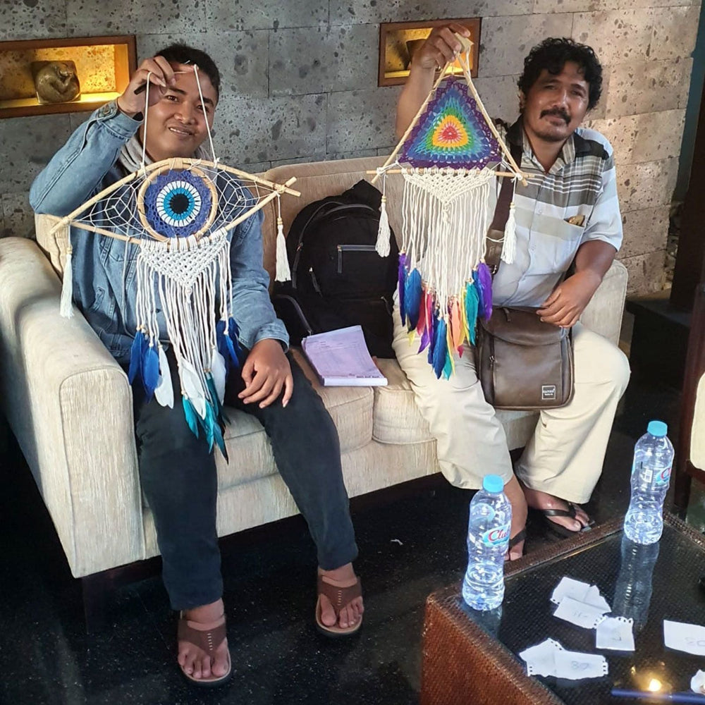 Two people sitting on a couch holding colorful dream catchers, with a table in front of them.