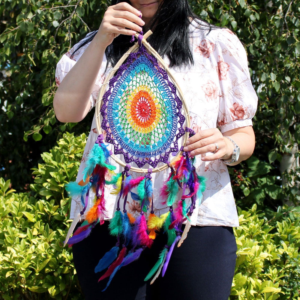 Person holding a colorful dreamcatcher against a green leafy background