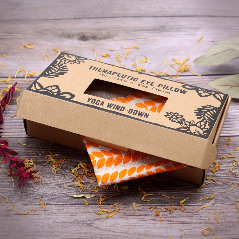 Therapeutic eye pillow in a cardboard box on a wooden surface with dried flowers.