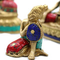 Decorative figurine of a seated figure with a blue mosaic disk, gold, red, and turquoise colors.