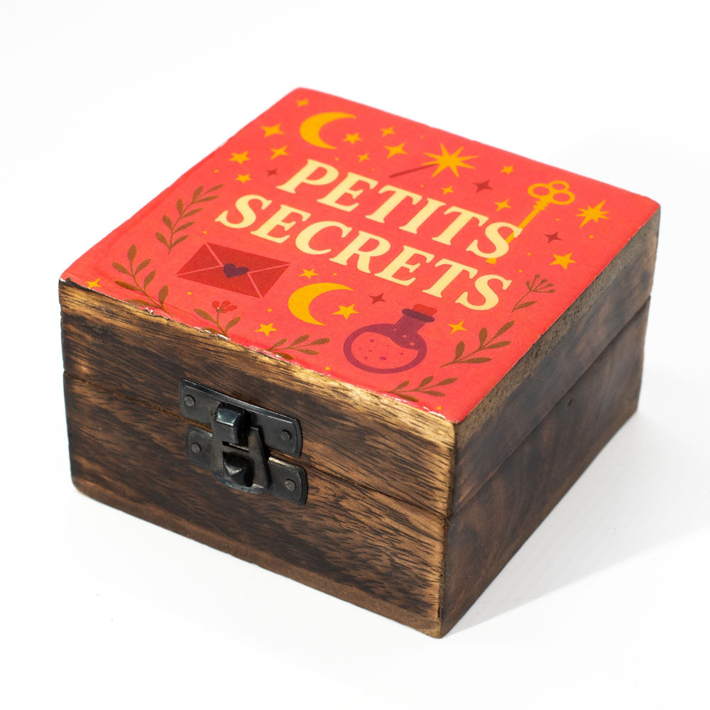 Wooden box with red lid featuring 'Petits Secrets' text and decorative elements on a white background