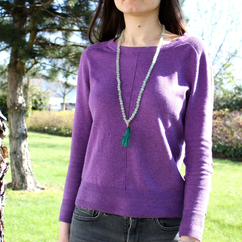 Person wearing a purple sweater with a necklace outdoors