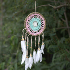 Dreamcatcher with pink and green circular design and white feathers against a blurred green background