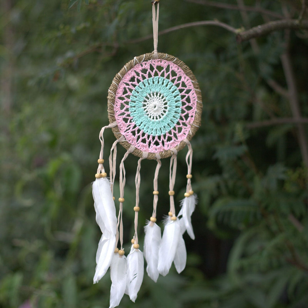 Dreamcatcher with pink and green circular design and white feathers against a blurred green background