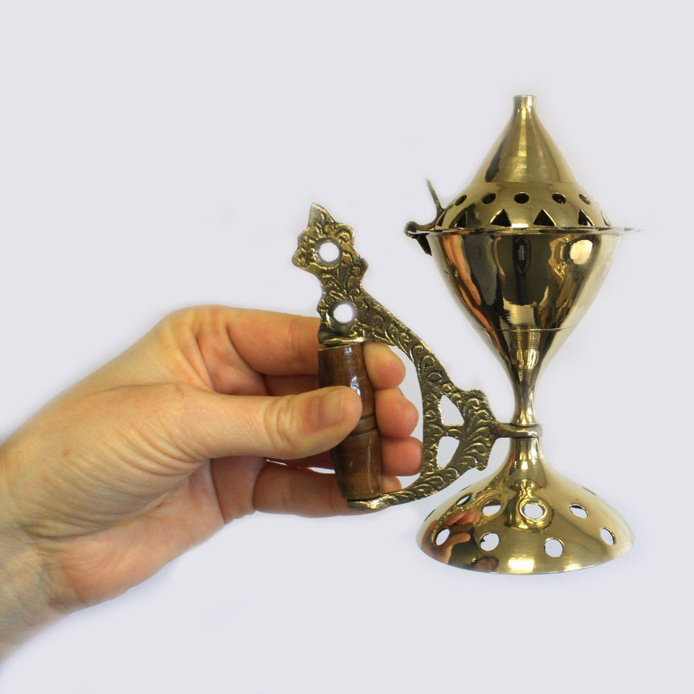 Hand holding a brass incense burner with a white background