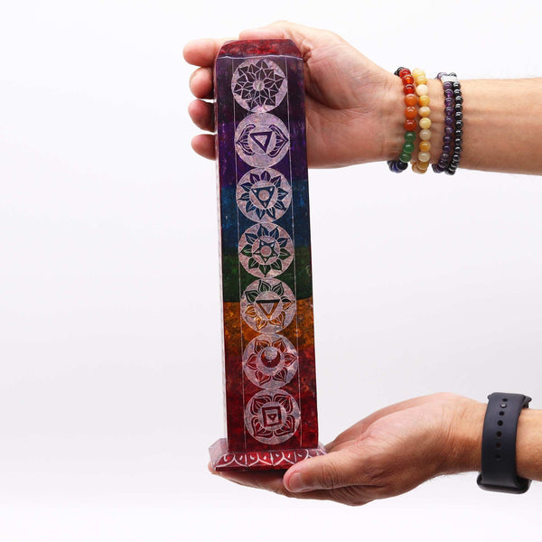 Hand holding a colorful crystal with chakra symbols against a white background