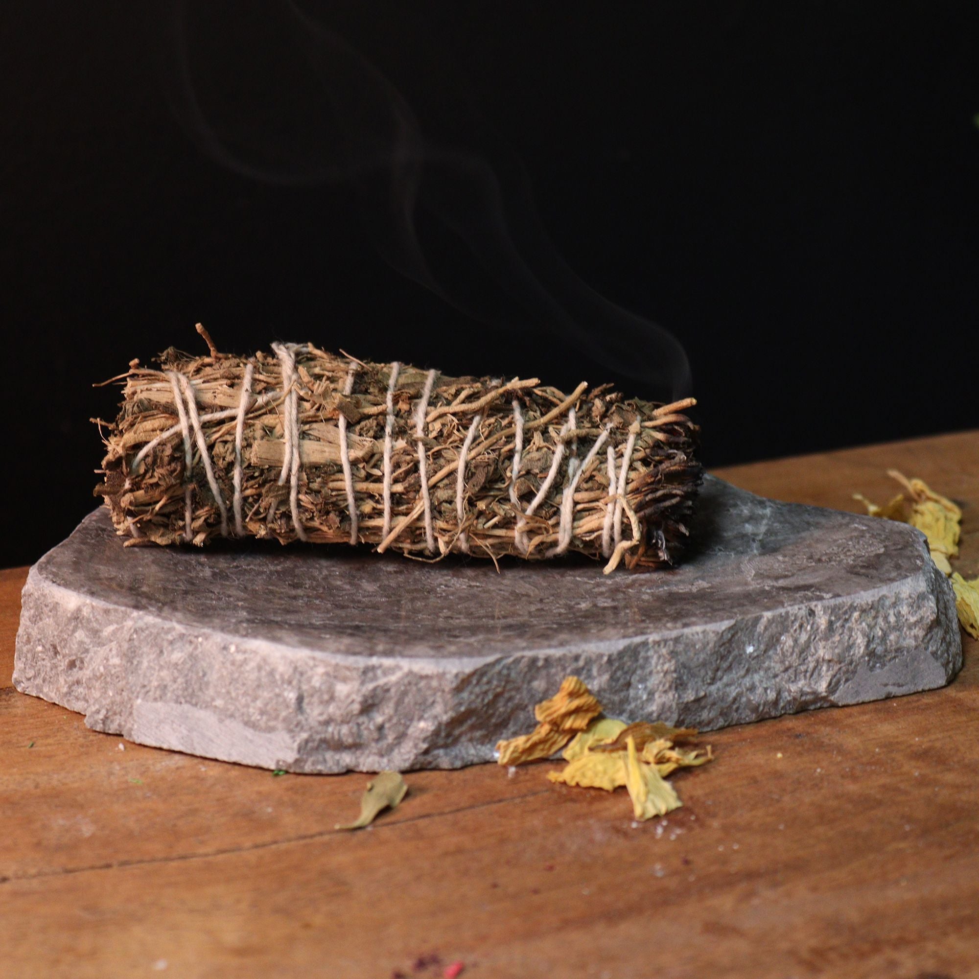 Bundled sage smoldering on a stone platform with a dark background