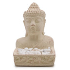 Stone sculpture of a Buddha bust with a small dish of white pebbles on a white background