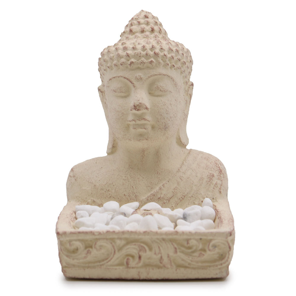 Stone sculpture of a Buddha bust with a small dish of white pebbles on a white background