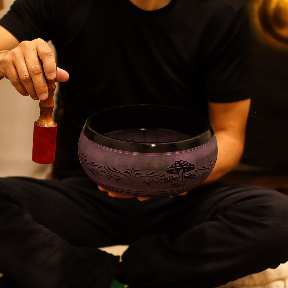 Person holding a purple singing bowl with a wooden mallet