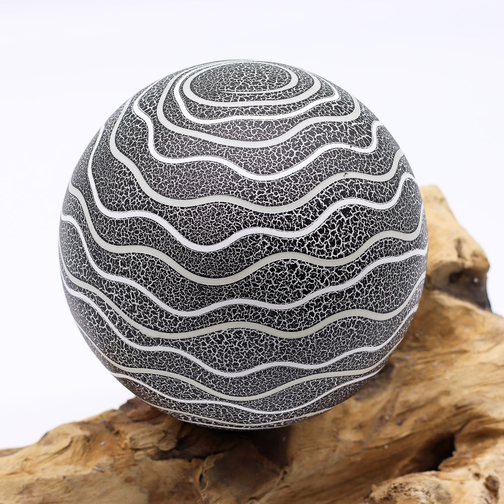 Decorative sphere with wavy pattern on a wooden surface