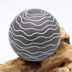 Decorative sphere with wavy pattern on a wooden surface