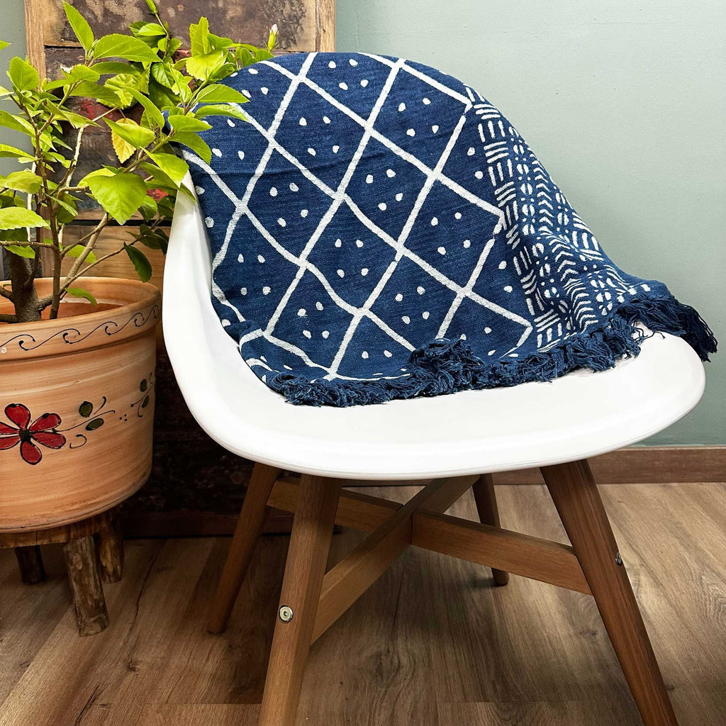Navy blue and white patterned blanket draped over a white chair with a wooden base, next to a potted plant.