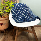 Navy blue and white patterned blanket draped over a white chair with a wooden base, next to a potted plant.