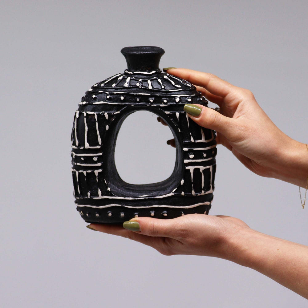 Person holding a black and white ceramic lantern against a gray background