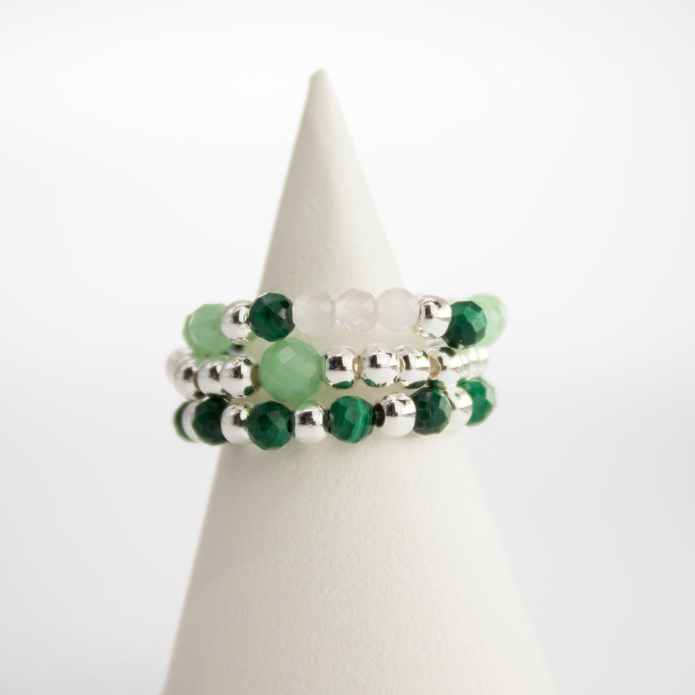 Stack of green and silver beaded bracelets on a white cone-shaped stand.