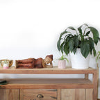 Wooden sideboard with decorative items including a plant, pots, and a leather bag on a white background.