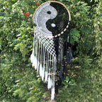 Dreamcatcher with yin yang symbol and feathers against a green leafy background