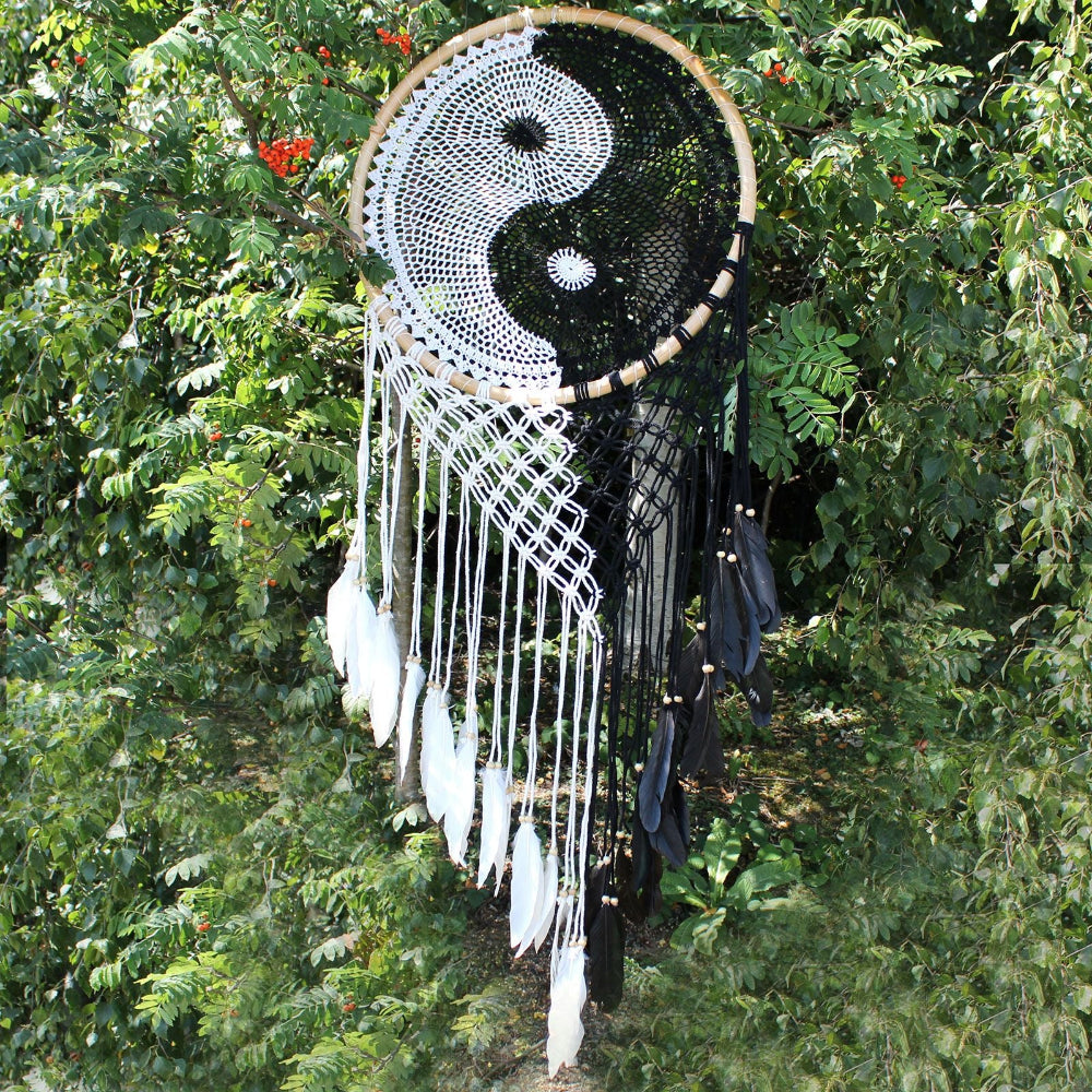 Dreamcatcher with yin yang symbol and feathers against a green leafy background