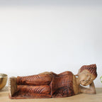 Wooden reclining Buddha statue on a wooden surface with a plain background
