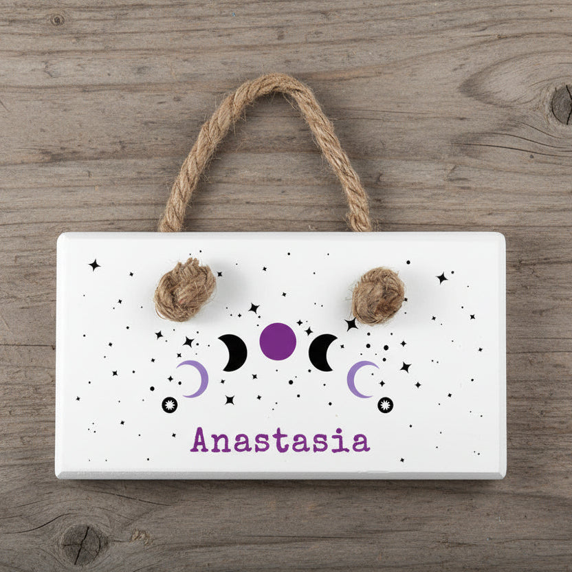 Decorative wall hanging with moon phases and the name 'Anastasia' on a light blue background.